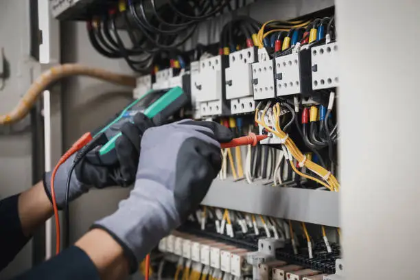 Technician inspecting corroded panel connections with meter and insulated tools, Electrician tracing circuit issues inside a Freehold - NJ basement using diagnostic tools